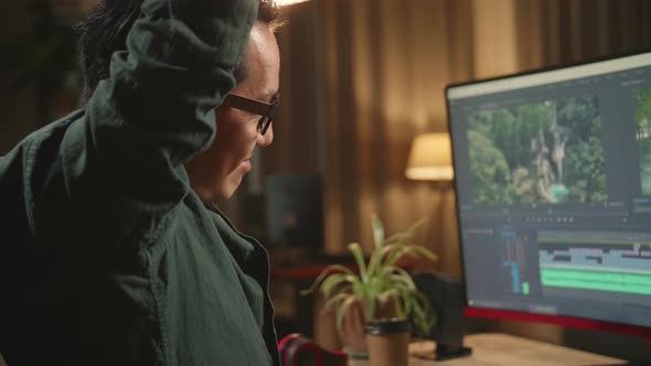 Asian Male Video Editor Stretching While Works With Footage And Sound On His Personal Computer