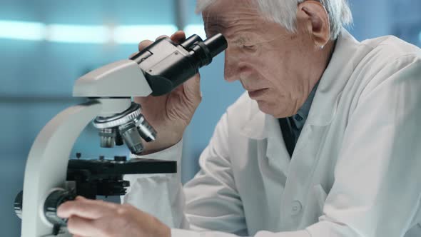 Elderly Scientist Using Microscope and Taking Notes