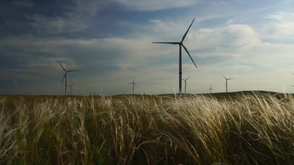 Motion the Blades of a Large Wind Turbine in a Field Against a Background of Cloudy Blue Sky with