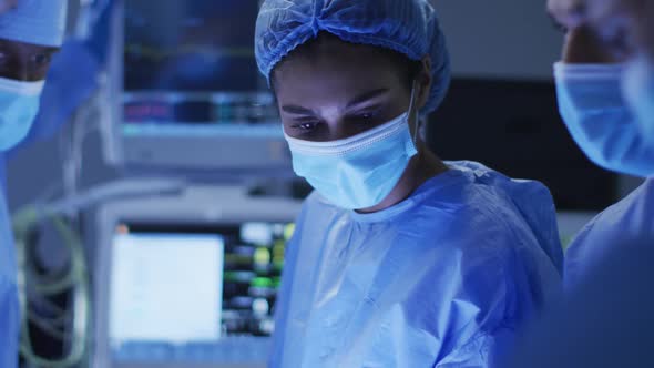 Mixed race surgeons wearing protective clothing discussing in operating theatre