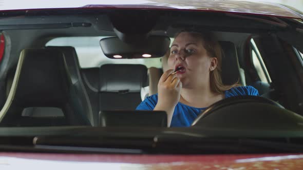 Young Obese Woman Putting on Lipstick in the Car Doing Makeup Behind the Wheel