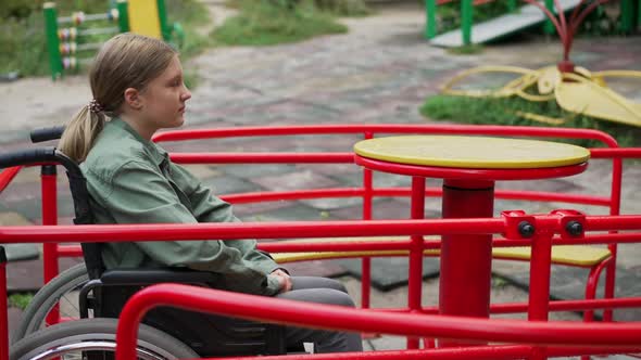 Lonely Sad Disabled Caucasian Girl in Wheelchair Spinning on Merry Go Round in Slow Motion