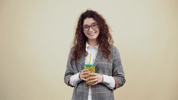 The Curlyhaired Teenager Smiles with Her Teeth Out While Holding a Yellow Glass of Fresh Juice