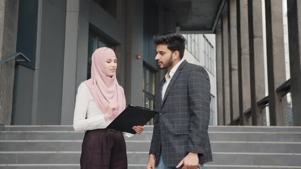 Arab Businessman Signing Papers on Clipboard That Holding Charming Woman in