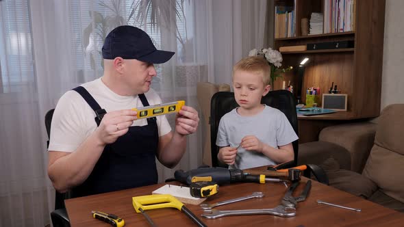 A Man in Overalls Teaches a Little Boy How to Use Various Tools for Repair