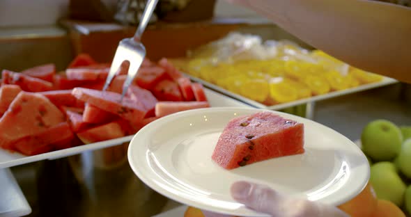 Person Puts Watermelon Slices on Plate with Silver Fork