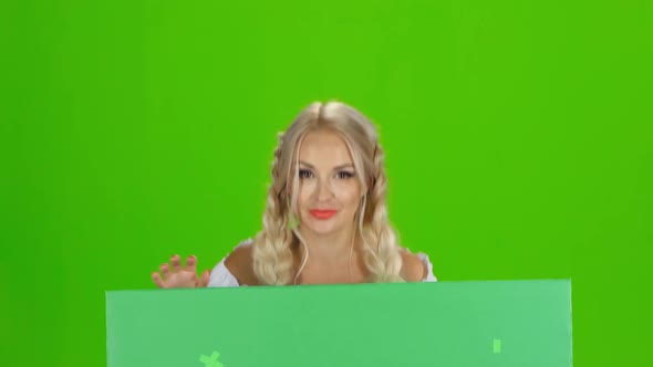 Bavarian Girl Looks Out From Behind the Green Board and Winking. Green Screen