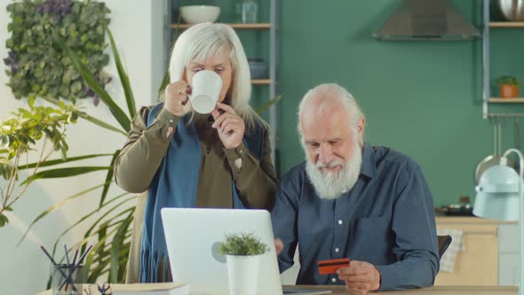 Happy Elderly Couple Shopping Online From Home Using Computer and Credit Card