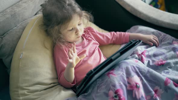 Portrait of Pretty Little Girl, a Child Who Lies on the Sofa Under the Blanket and Plays on Tablet