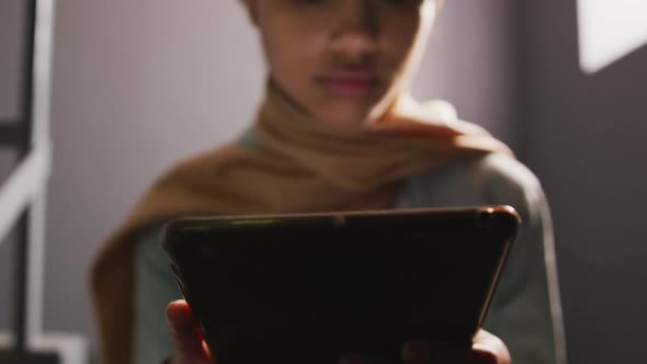 Asian female student wearing a beige hijab sitting on stairs and using a tablet