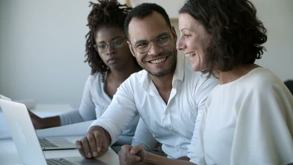 Group of Smiling Workers Talking and Pointing at Laptop