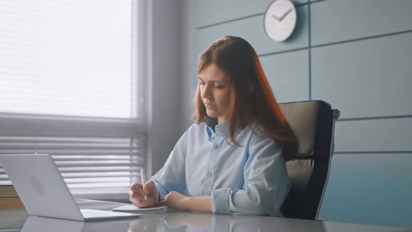 Concentrated young woman doctor writes in paper notebook