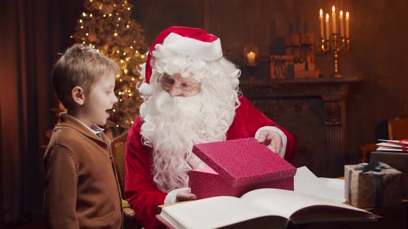 Santa Claus and little boy. Cheerful Santa is working at the table. Christmas concept.