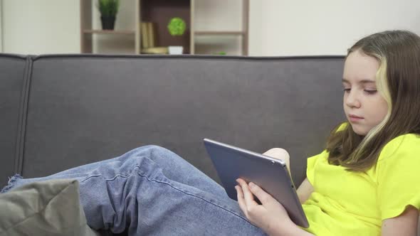 A Little Girl Touches a Tablet While Lying on the Couch at Home