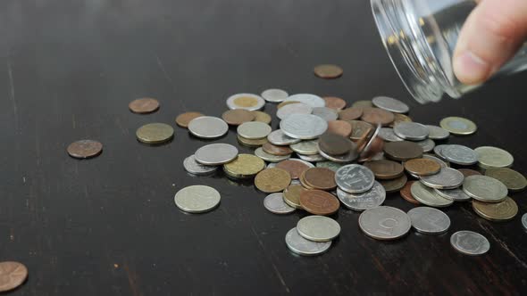 Stack of coins are falling on table from glass jar 