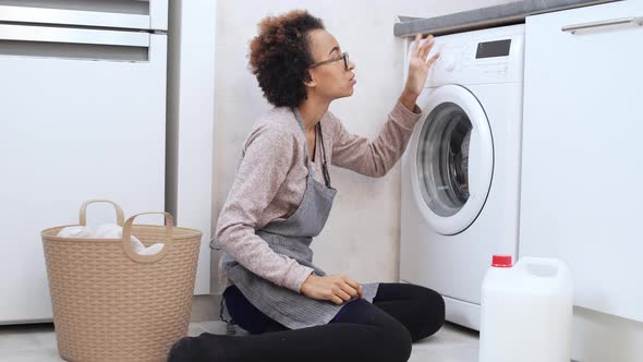 Mixedup Young Dark Skinned Female in Glasses and Apron Sitting on Floor Trying to Understand How to