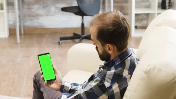 Over the Shoulder Shot of Young Man Looking at Green Screen Phone