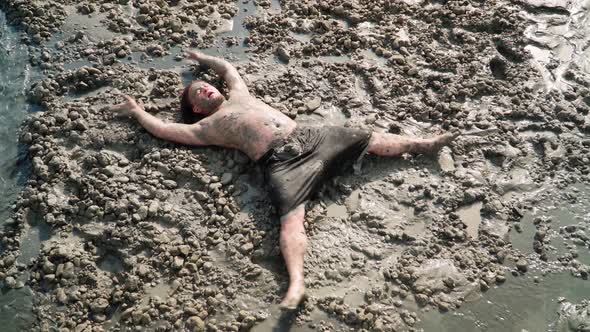 Funny Fat Man with Long Hair Lies and makes an Mud Angel. Overhead shot