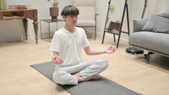 Asian Man Meditating on Yoga Mat at Home