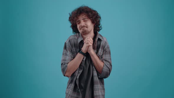 Young Hipster Asks for Help Praying with His Hands Together in the Studio on a Turquoise Background