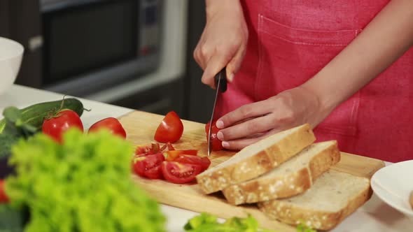 close up of female hand cutting tomato on board in kitchen room