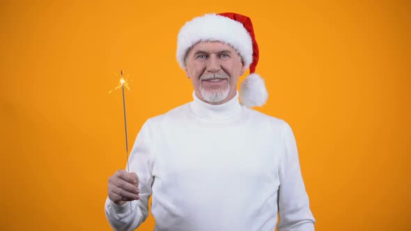 Joyful Elderly Person in Santa Claus Hat With Bengal Light Smiling on Camera