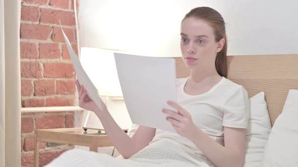 Hardworking Young Reading Documents in Bed