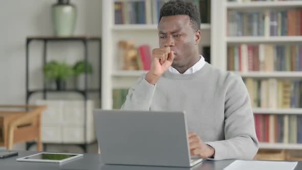 African Man Coughing While Using Laptop in Library