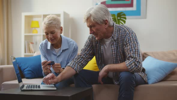 Happy Mature Couple Sitting on Sofa and Doing Online Shopping on Laptop