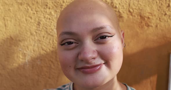 Bald girl posing and smiling in front of camera with yellow background