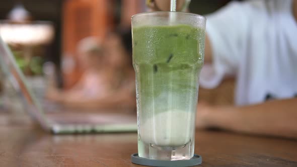 Close Up of Metal Straw Stirring Matcha Ice Tea Latte with Almond Milk