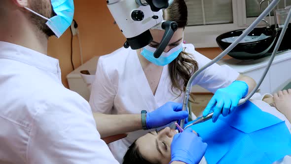 Dentist with assistant under microscope treats the patient's teeth. Modern progressive dentistry.