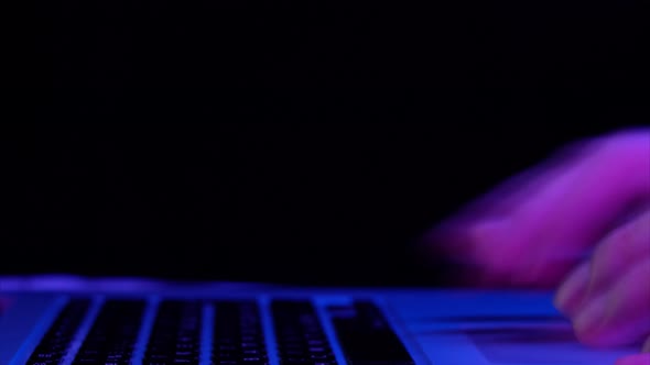 Man Types on Laptop Keyboard at Neon Purple Illumination