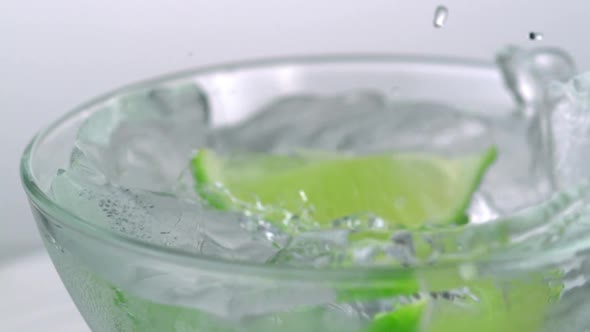 Slo-motion lime wedges into ice cube filled glass