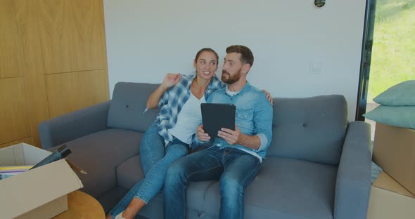 Happy Couple Renters Owners Tenants Sit on Sofa Use Digital Tablet on Moving Day in New House, Man