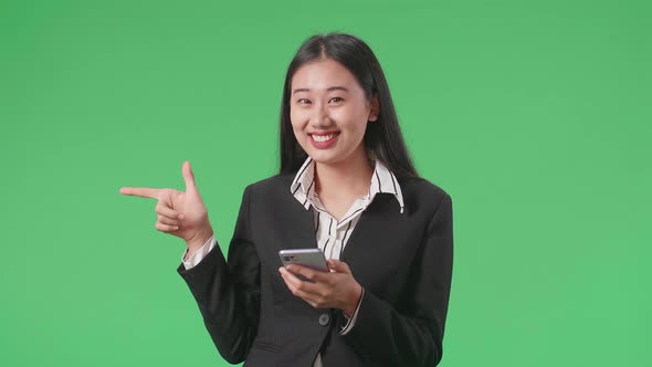 Business Woman Flipping Through Mobile Phone With A Smile Pointing To The Side In The Green Screen