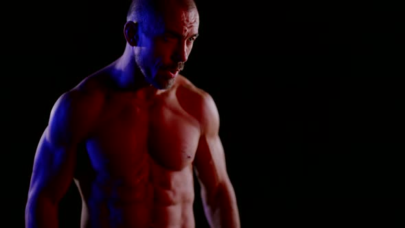 a Muscular Man with a Naked Torso Lowers Arms Stands Then Strikes Against a Dark Background