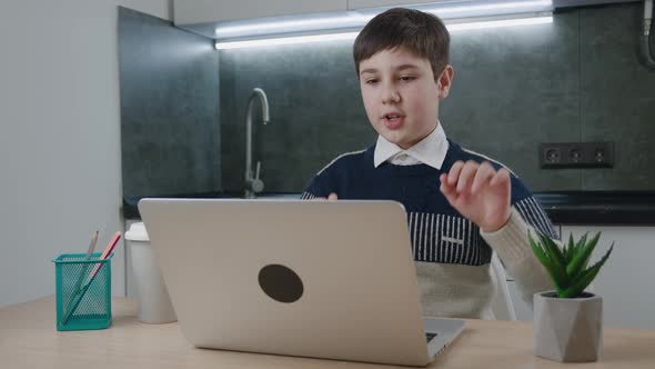 Smiling Boy Chatting Online By Video Call with Laptop Computer at Home While Sitting at the Table