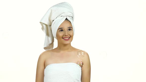 Girl in White Towel on Her Head with a Charming Smile Watches the Soap Bubbles Isolated on White