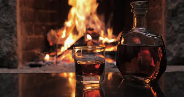 Bottle and Glass with Whiskey or Cognac on the Background of Fire in the Fireplace