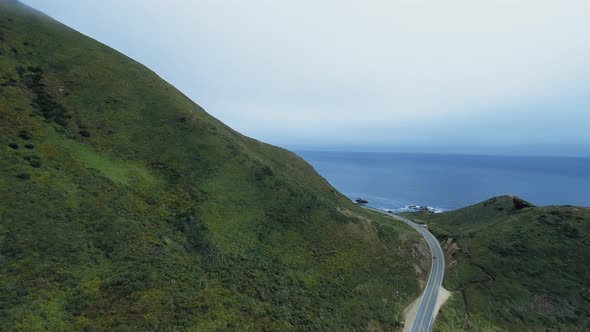 Aerial shot of road going thorugh green hills near the ocean in Garrapata, California, USA