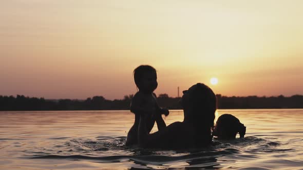 Mom Plays with a Naked Baby in Oversleeves in the Lake Against the Background of a Summer Sunset