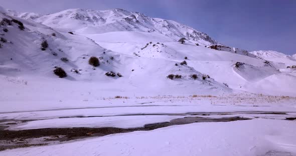 Fly Over Attractive Frozen River And Mountains Covered With White Snow During A Clear Day With Narro