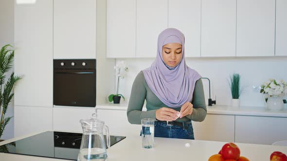 Progressive Arab Woman in a Hejab and Jeans Drinks Vitamins or Medicines in Her Kitchen