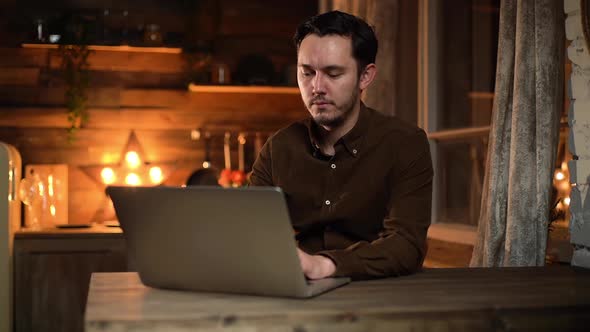 Attractive Man in Casual Clothing Typing on Laptop While Sitting at the Table.