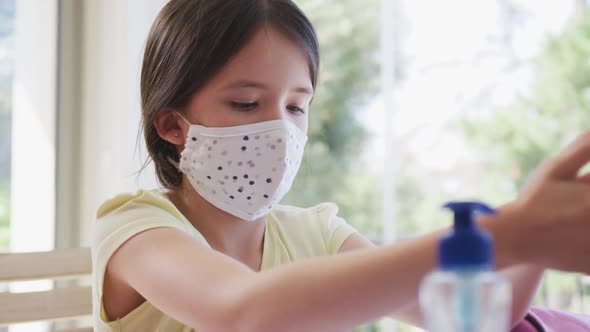 Girl wearing face mask sanitizing her hands at home