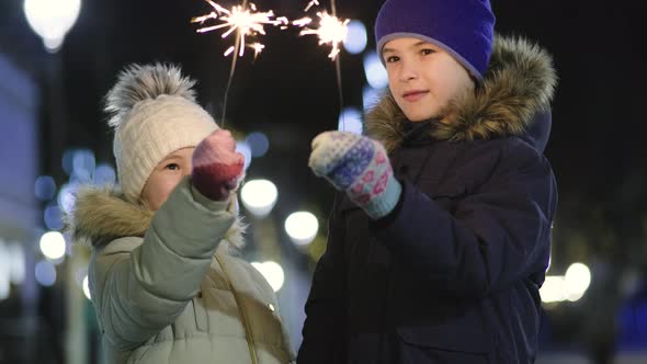 Two cute young children, boy and girl in warm winter clothing holding burning sparkler fireworks 