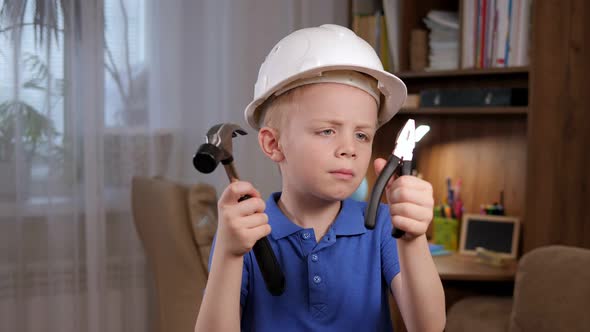 Portrait of a Small Surprised Boy in a Helmet with Tools in His Hands at Home