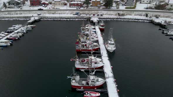 Fishing boats anchored in Arctic harbor, fresh snow of winter, drone dolly out