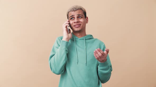 Handsome curly-haired man wearing blue hoodie talking by phone